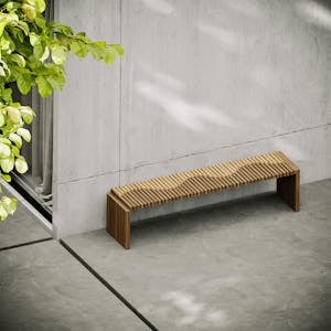 A sleek wooden bench placed outdoors against a concrete wall with foliage overhead.