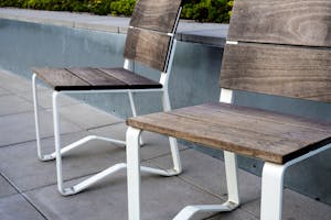 Pair of wooden and metal chairs on a concrete patio with greenery in the background.