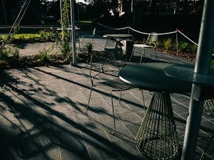 Shadowed outdoor patio area featuring modern wireframe tables and chairs.