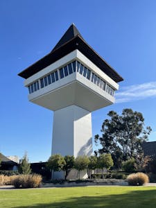 Tall modern tower with geometric design set against a clear blue sky and garden.